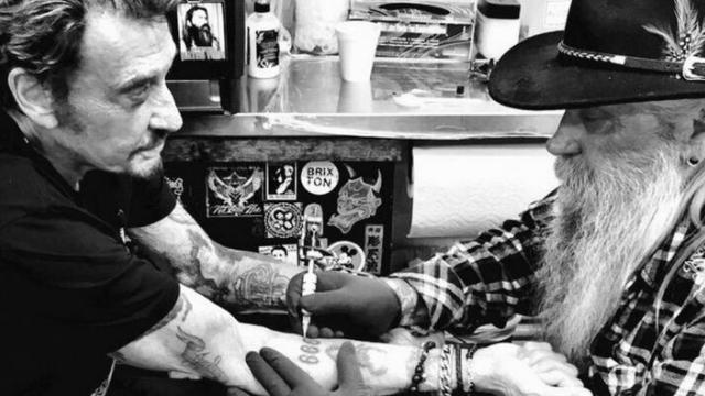 Johnny Hallyday en train de se faire tatouer le nombre 666 sur son avant-bras droit en 2014