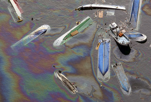 Coques de navires retournés flottant dans une eau de mer mazoutée à Fudaï.