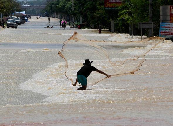 pécheur jetant sa nasse dans une rue inondée en Thaïlande