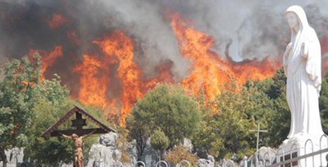 Flammes menaçant un crucifix et la statue de la Vierge   sur la colline des apparitions à Medjugorje (Bosnie-Herzégovine)